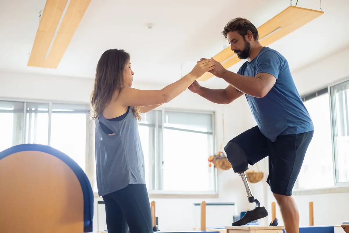 Paciente con una prótesis de pierna haciendo un ejercicio de equilibrio de la mano de su fisioterapeuta